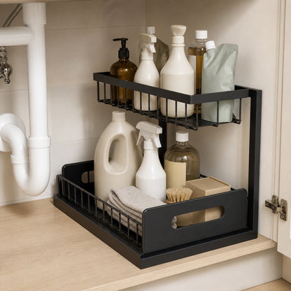 Black metal two-tier organiser holding detergent bottles and cloths under a sink, with the lower basket pulled out