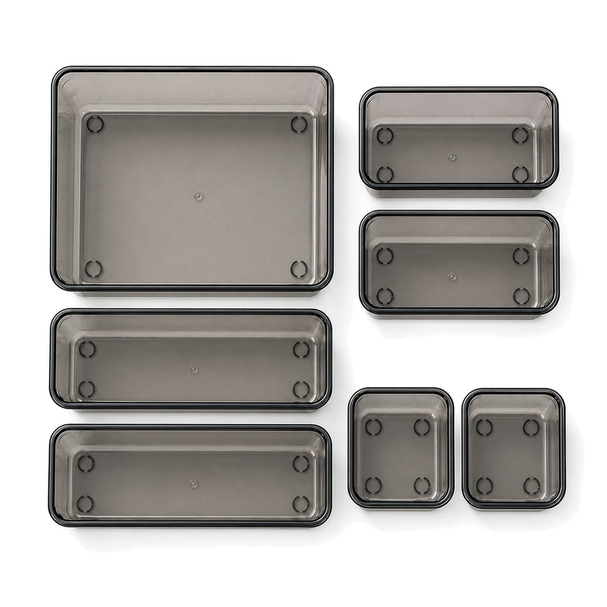 Seven transparent-black modular drawer trays in four sizes, arranged on a white background