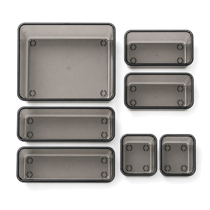 Seven transparent-black modular drawer trays in four sizes, arranged on a white background